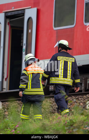 24 agosto 2019, Sassonia, Bad Schandau: due vigili del fuoco del volontario vigili del fuoco Stadt Königstein a piedi lungo il convoglio. Nello scenario dell'esercitazione si ipotizza che una grave situazione di tempesta con forti precipitazioni e tempeste prevarrà nella zona della capitale dello stato di Dresda come pure nei distretti di Bautzen e sassoni Switzerland-Osterzgebirge per diversi giorni. Intorno a 5 p.m., un treno EC con 300 passeggeri sarà in viaggio verso Praga nella valle dell'Elba, vicino al confine con la Repubblica ceca, dove sarà colpito da una frana causata dalla pioggia persistente che ha buri Foto Stock