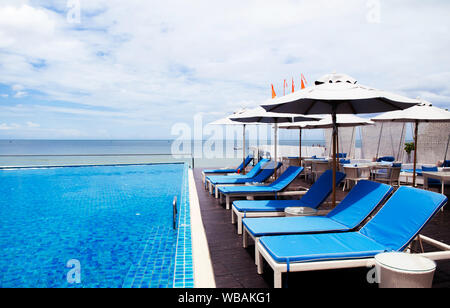 Ago 6, 2014 Hua Hin, Thailandia - piscina sulla spiaggia con blue lettino in spiaggia e ombrelloni bianchi, resort tropicale spazio all'aperto in estate Foto Stock