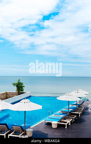 Ago 6, 2014 Hua Hin, Thailandia - piscina sulla spiaggia con blue lettino in spiaggia e ombrelloni bianchi, resort tropicale spazio all'aperto in estate Foto Stock