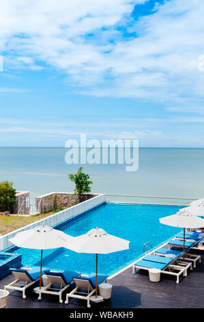 Ago 6, 2014 Hua Hin, Thailandia - piscina sulla spiaggia con blue lettino in spiaggia e ombrelloni bianchi, resort tropicale spazio all'aperto in estate Foto Stock