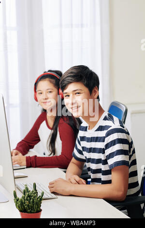 Allegro mixed-gara adolescenti seduti alla scrivania in classe e di programmazione sulla riproduzione su computer Foto Stock