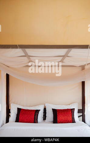 FEB 25, 2014 Dalat, Vietnam - tropicale asiatico parete gialla camera da letto in legno con letto a baldacchino tenda bianca e coloratissimi cuscini. Foto Stock