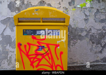 Orange graffitis su un giallo francese casella postale attaccato ad una parete spiovente con crepis Foto Stock