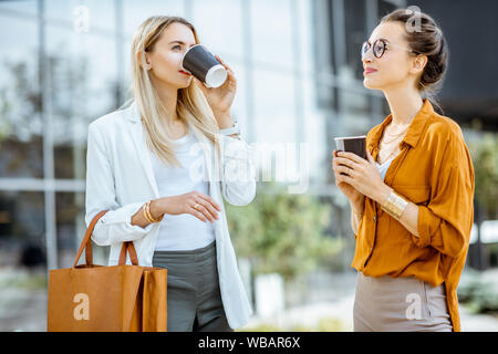 Due giovani imprenditrici parlando vicino all'edificio per uffici, avente una piccola conversazione durante la pausa caffè all'aperto. Foto Stock