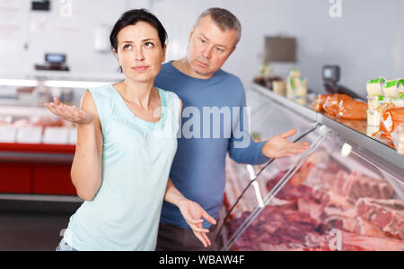 Triste adulto giovane ai clienti la scelta di carne in macelleria Foto Stock