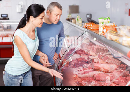 Felice coppia ai clienti la scelta di carne e di discutere in macelleria Foto Stock