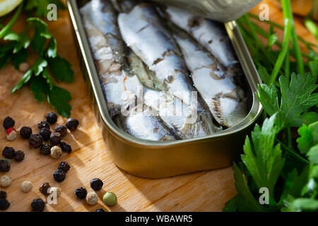 Vista ingrandita di aperto può affumicato sardine in olio su tavola di legno con prezzemolo fresco, limone e spezie Foto Stock