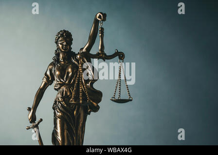 Statua di ottone di una giustizia bendati tenendo le bilance e la spada su un laureato sfondo grigio e copiare lo spazio in una immagine concettuale Foto Stock