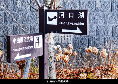 30 NOV 2018 Kawaguchiko, Giappone - Lago Kawaguchiko e vista Komagari Plaza cartello in legno informazioni di direzione con giardino e il muro di pietra sullo sfondo Foto Stock