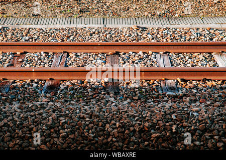 Vecchio grungy rusty binario ferroviario con traversa di legno e di pietra sotto la luce del sole con qualche parte in ombra Foto Stock