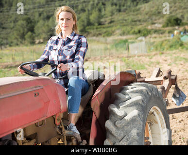 Donna sorridente agricoltore lavora sul trattore agricolo nel suo smallholding Foto Stock