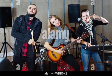 Tre lieti compagni di band che pongono insieme con gli strumenti musicali in sala prove Foto Stock