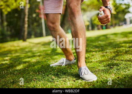 Close-up di uomo di gambe essendo spruzzato con repellente per insetti nel parco all'aperto Foto Stock