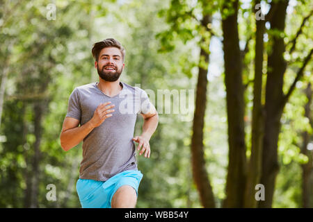 Felice giovane jogging all'aperto in un parco in estate Foto Stock