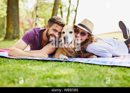 Coppia giovane avente un picnic con il loro cane nel parco, giacente sulla coperta e guardando la fotocamera Foto Stock