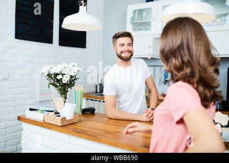 Allegro barista in piedi dietro il contatore e facendo ordine dal cliente femmina Foto Stock