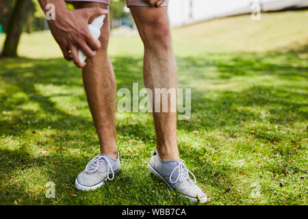 Close-up di un uomo la spruzzatura di repellente per insetti sulle gambe mentre all'aperto Foto Stock