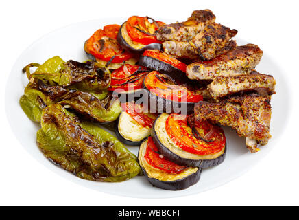 Arrosto di costolette di maiale servita con verdure grigliate sulla piastra bianca. Isolato su sfondo bianco Foto Stock