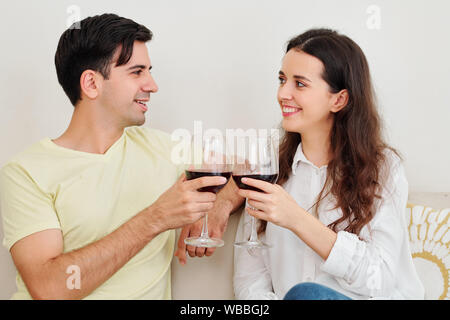 Sorridente ragazzo e ragazza la tostatura con bicchieri di vino e guardando ogni altro quando aventi data a casa Foto Stock