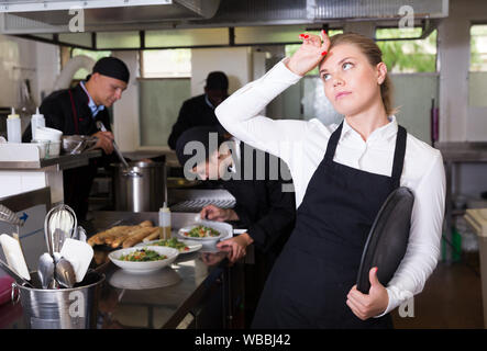 Infelice e stanco giovane cameriera in attesa ordinato piatti nel ristorante cucina Foto Stock