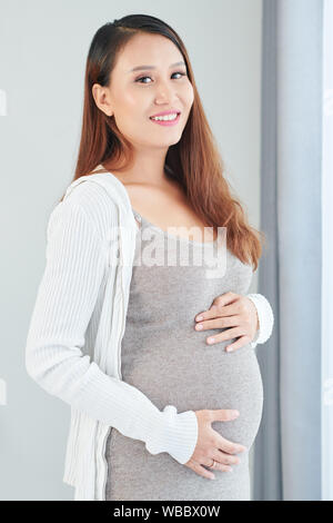 Immagine ritagliata della giovane bella incinta Donna vietnamita di toccare la sua grande pancia e guardando la fotocamera Foto Stock