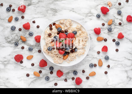 Fiocchi d'avena sana servita con frutti di bosco, scaglie di cioccolato e mandorle e miele su una tavola di marmo dello sfondo. Scattato dalla vista dall'alto. Foto Stock