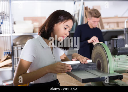 Focalizzato ragazza brasiliana lavorando sulla macchina rettificatrice, preparare i dettagli per modello architettonico in officina dello studente Foto Stock