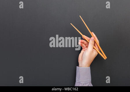 Immagine creativa delle bacchette di legno nelle mani di sesso maschile su sfondo nero. Il giapponese e il cinese del cibo con copia spazio. Foto Stock