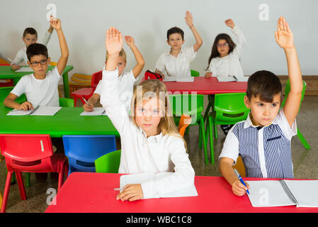 Gruppo di allievi che studiano insieme nella scuola elementare, alzando le mani per rispondere Foto Stock