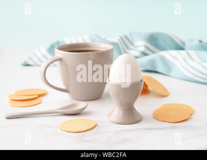 Uovo sodo in ceramica tazza di uovo, una tazza di caffè e sottili e croccanti patatine di mais su sfondo di turchese asciugamano da cucina. Concetto di colazione. Copia dello spazio. Foto Stock