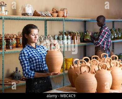 Sorridente lavoratore di sesso femminile che di laboratorio di ceramica di argilla di disporre le merci sugli scaffali per la vendita Foto Stock