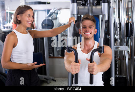 I giovani ben addestrati uomo utilizzando pec deck palestra macchinari mentre ascolto la fidanzata in ambienti interni Foto Stock