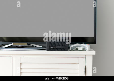 Flat TV LCD sul cabinet bianco in salotto con il grigio scuro muro. Video gaming console e gamepad. Stazione di videogamer mockup Foto Stock