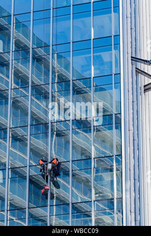 Due uomini che si abbellono o si abbellono e lavorano su una tenda di vetro all'esterno di una nuova torre per uffici a più piani a Sydney, Australia Foto Stock