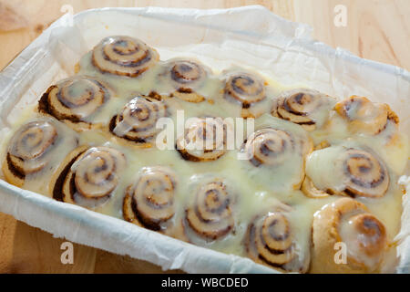 Appena sfornato cinnabons fatti in casa panini alla cannella con latte glassa di zucchero in una teglia Foto Stock