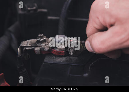 Man mano si serra il dado con una vecchia chiave. La sostituzione della batteria presso il garage. Primo piano. Foto Stock