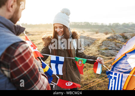 Felice coppia giovane vestito in abiti caldi pitching una tenda al campo Foto Stock