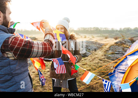 Felice coppia giovane vestito in abiti caldi pitching una tenda al campo Foto Stock