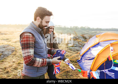 Felice coppia giovane vestito in abiti caldi pitching una tenda al campo Foto Stock