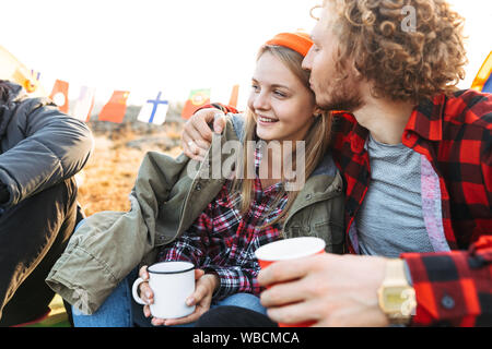 Il gruppo di allegro giovani amici camping all'aperto, seduta con tazze e thermos Foto Stock