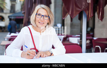 Ritratto di eleganti donna matura chi scrive documenti in tempo utile il pranzo con caffè Foto Stock
