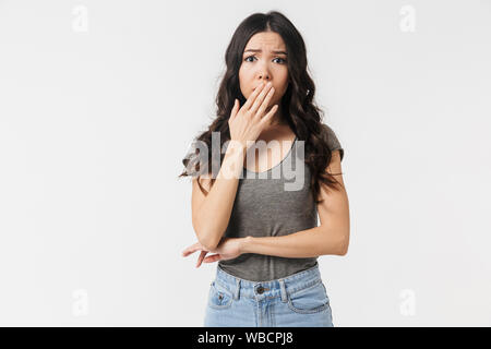 Immagine di orinato brunette donna 20s vestito in abiti di base preoccupante e bocca di copertura isolato su sfondo bianco Foto Stock