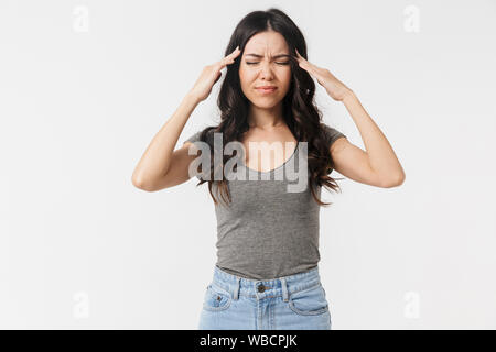 Immagine di esaurito brunette donna 20s vestito in abiti di base afferrando la sua testa isolate su sfondo bianco Foto Stock