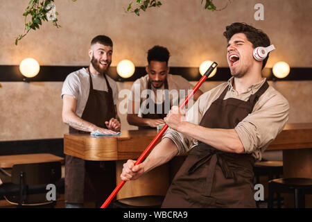 Tre uomini allegra baristi presso la caffetteria cafe di pulizia al termine di una giornata di lavoro Foto Stock