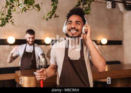 Tre uomini allegra baristi presso la caffetteria cafe di pulizia al termine di una giornata di lavoro Foto Stock