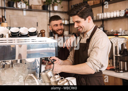 Il gruppo di allegro uomini baristi indossando grembiuli lavorando presso il contatore in cafe indoor, parlando Foto Stock