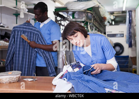 Focalizzato donna che lavorano nella moderna lavanderia, controllo qualità dei panni di pulizia Foto Stock