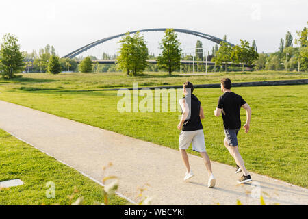 Immagine di due uomini muscolare in sportswear lavorando fuori e in esecuzione al green park all'aperto in mattinata Foto Stock