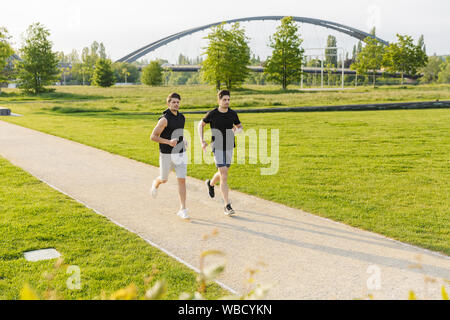 Immagine di due uomini concentrato in sportswear lavorando fuori e in esecuzione al green park all'aperto in mattinata Foto Stock