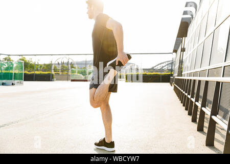 Immagine dell uomo muscolare in sportswear Indossa auricolari formazione sul campo sportivo durante la mattina allenamento all'aperto Foto Stock